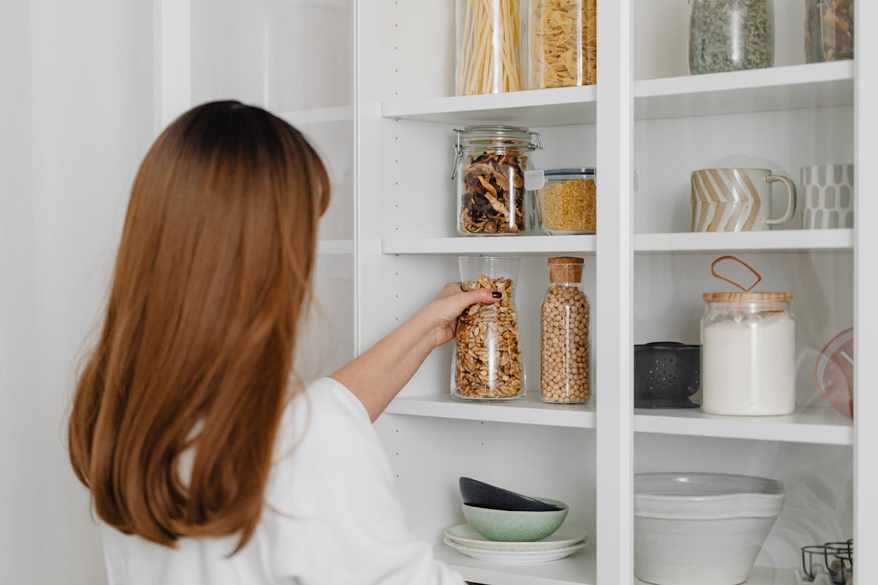 a woman in a white shirt holding a clear glass jar with nuts stored in a pantry