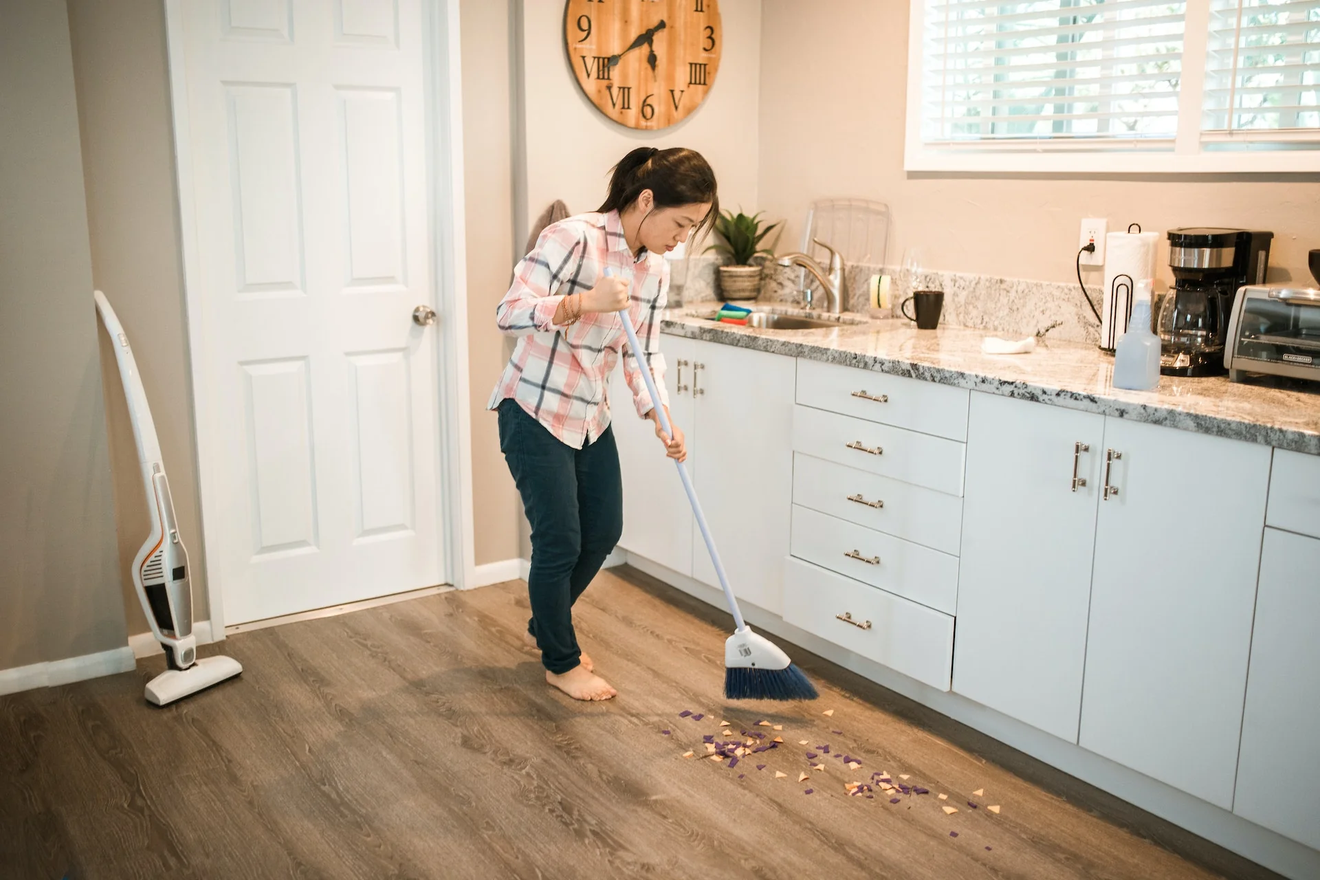 A woman sweeping a kitchen floor with a white broom