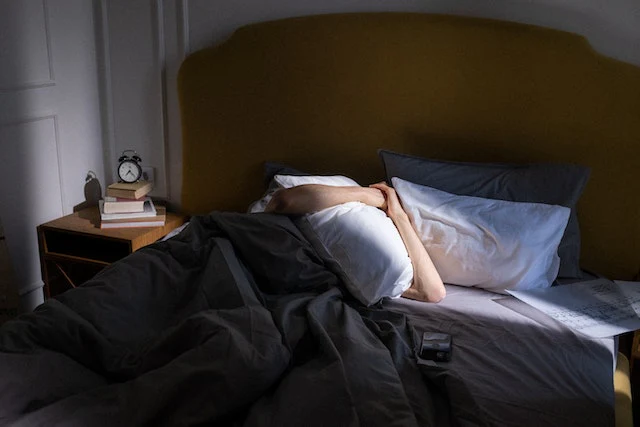 Woman lying on bed covered with black blanket
